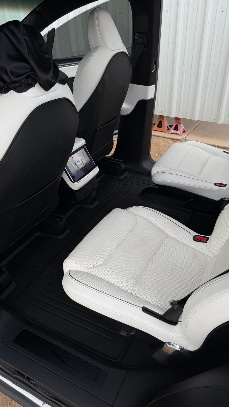 Car interior with white and black custom seat covers installed on front and rear seats, door open to metal warehouse building