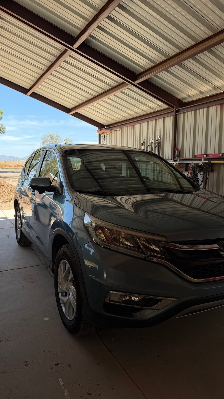 Black SUV parked under metal carport with corrugated roof panels and open rural landscape visible in background